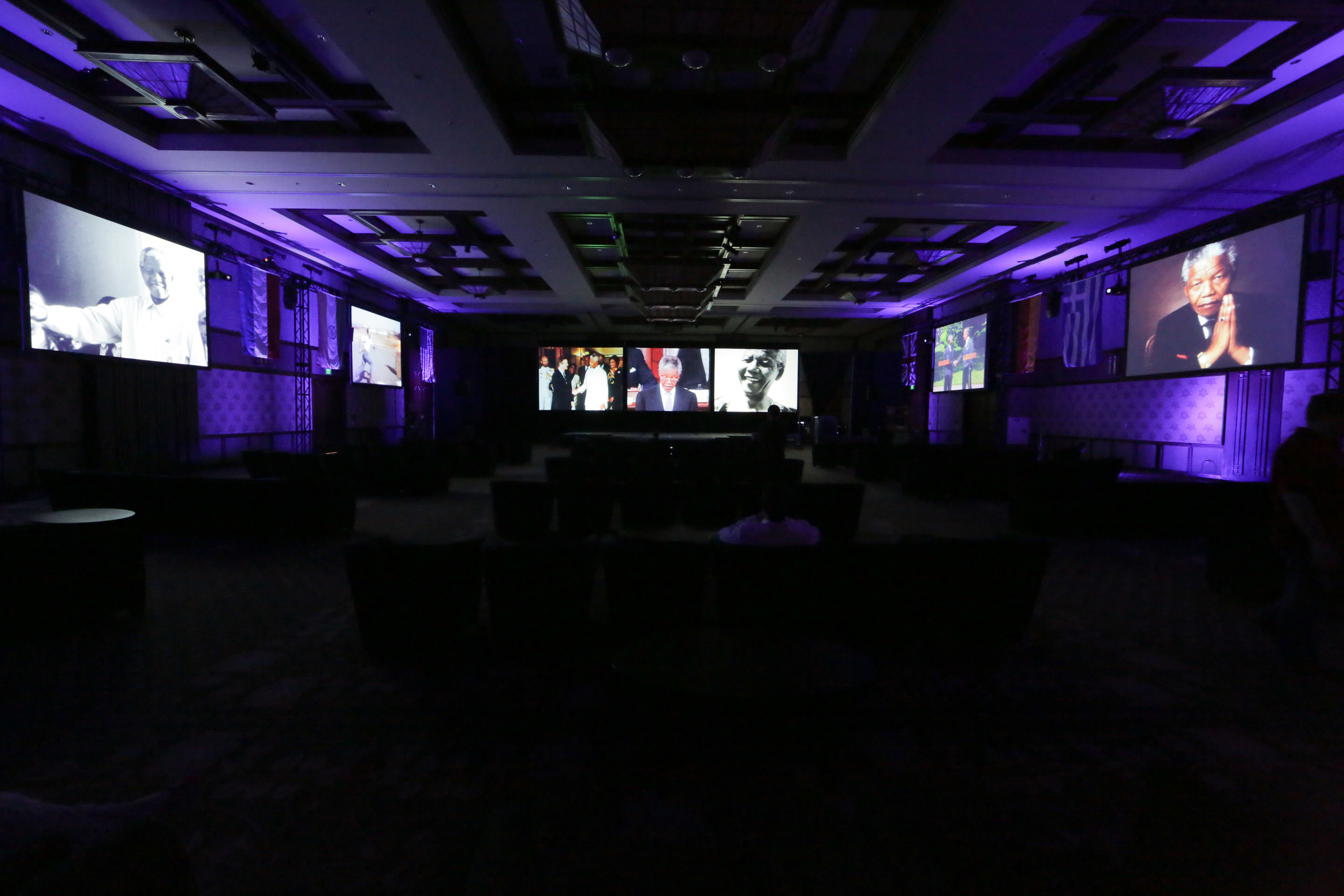 A view of how Tri-Marq set up the Disneyland Grand Californian ballroom for a recent event. There are projector screens lining each side wall and a large screen in the front of the house with uplighting on both sides.