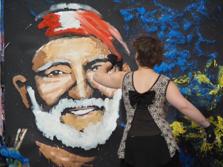 One of the three painters in action. She is painting a man with a white beard with a red bandana.