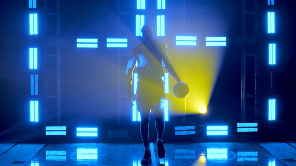 For gallery page: A still from the Marquette Basketball intro video for sports marketing. The player is dribbling the ball in front of the lit up background.