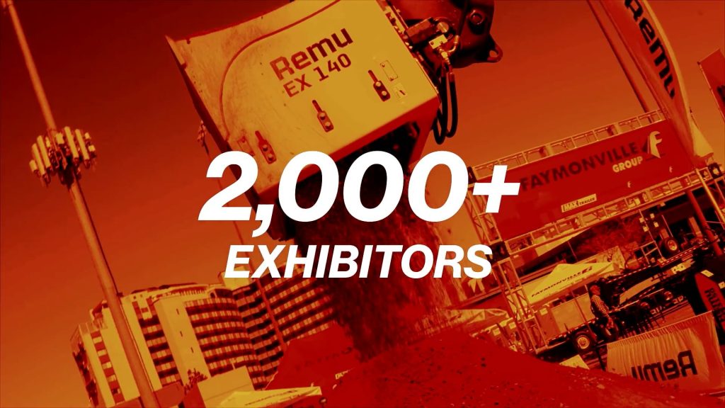 For gallery page: A thumbnail from the Conexpo-Con/Agg recap video. Features a machine dumping soil for a demonstration with a translucent green overlay and "2000+ Exhibitors" motion graphics superimposed on top of the shot. 