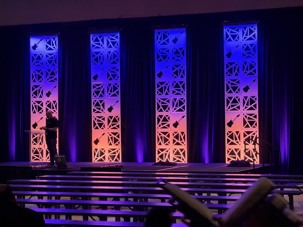 For gallery page: A view from back-of-house at the AHTD 2026 Spring Conference in Nashville, Tennessee. Features a view of the enhances set columns lit in sunset colors.