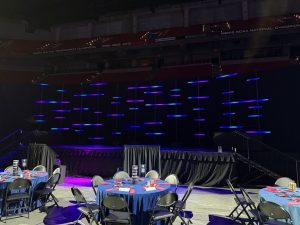 A view from back-of-house at the 2026 GMCC icebreaker event at the Kohl Center in Madison, Wisconsin. Features the titan tube stage setup in purple and blue hues.