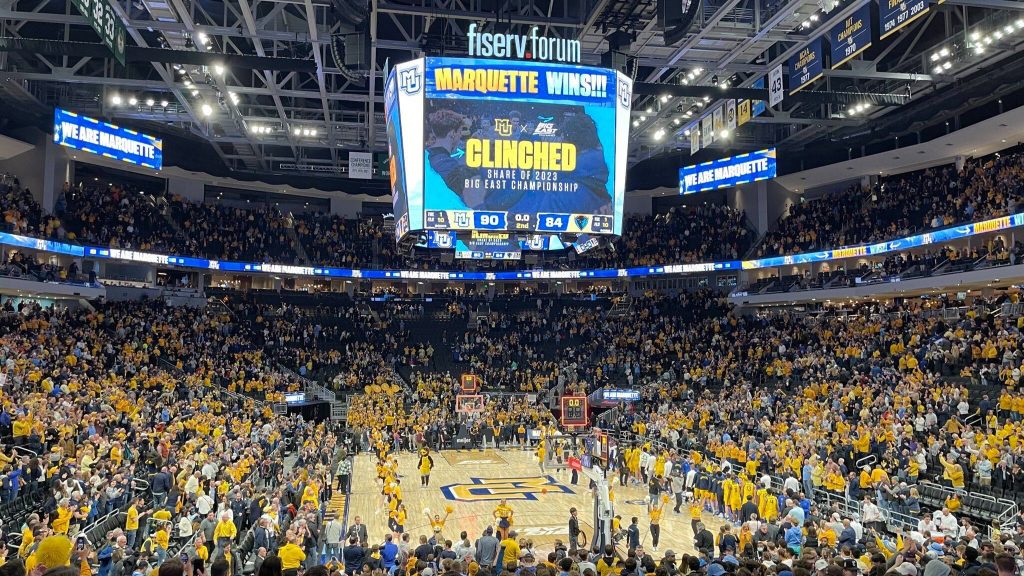 A courtside view of the Fiserv Forum jumbotron featuring MUBB graphics