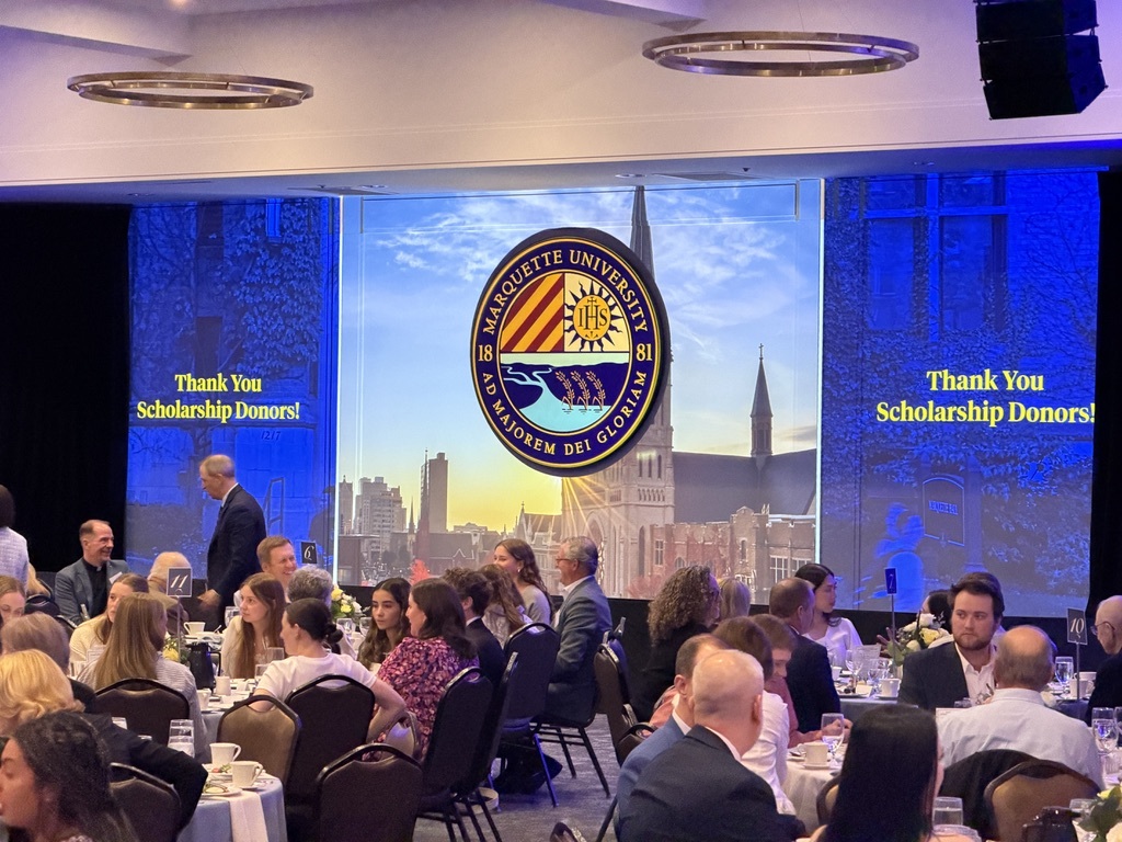 For gallery page: A photo from the Marquette University Scholarship Event. Features a photo of the projector wall setup from back of house. "Thank you scholarhip donors" is projected on either side of the main center screen. 