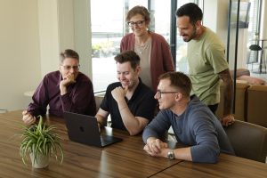 A group of employees gathered in an office setting around a laptop.