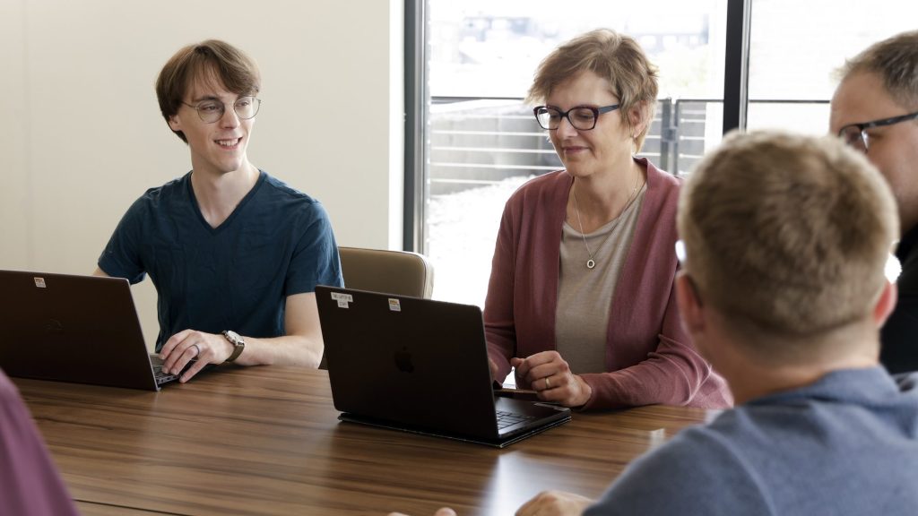 Tri-Marq production coordinator, Jen Harper, sits at a conference table with other crew members working on a project.